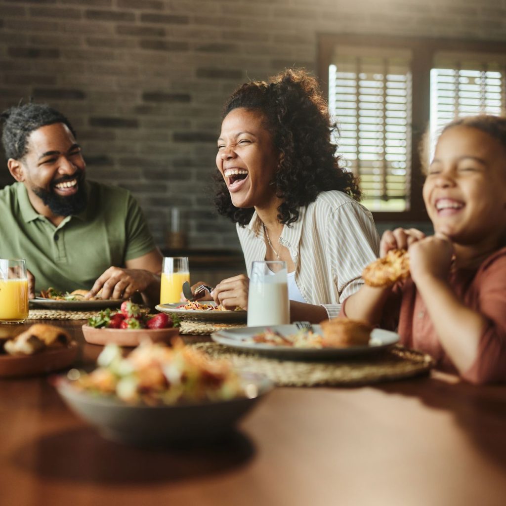 Family laughing and enjoying a meal together at a dining table with drinks and food.